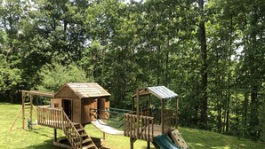 A wooden playground with a slide and climbing structures, surrounded by a grassy area and trees. - Unique home in great neighborhood (Stroudsburg)