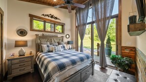 A bedroom with a large bed, a ceiling fan, a nightstand with a lamp, and a window with curtains. - Red Wolf Chalet -Tiny Home with Eagles Nest amenities, private fire pit, pet friendly (Banner Elk)