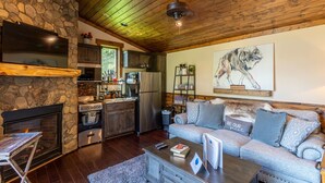 A cozy living room with a fireplace, a stone wall, a wooden ceiling, and a sofa with cushions. - Red Wolf Chalet -Tiny Home with Eagles Nest amenities, private fire pit, pet friendly (Banner Elk)