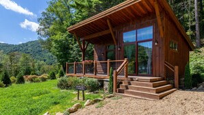 A wooden cabin with a balcony, surrounded by lush greenery and a mountain backdrop. - Red Wolf Chalet -Tiny Home with Eagles Nest amenities, private fire pit, pet friendly (Banner Elk)