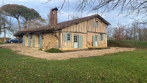 Une maison traditionnelle à colombages, avec des fondations en pierre, une cheminée et une allée gravillonnée.