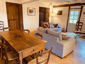 Un coin repas avec une table et des chaises en bois, un canapé gris et une petite table d’appoint avec une lampe.