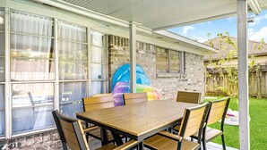 Eine überdachte Terrasse mit Holztisch und -stühlen, einer großen aufblasbaren Rutsche und einer Ziegelwand.