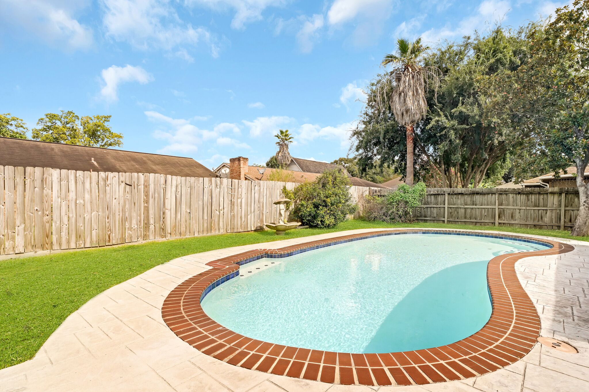 A backyard with a swimming pool, wooden fence, and trees.