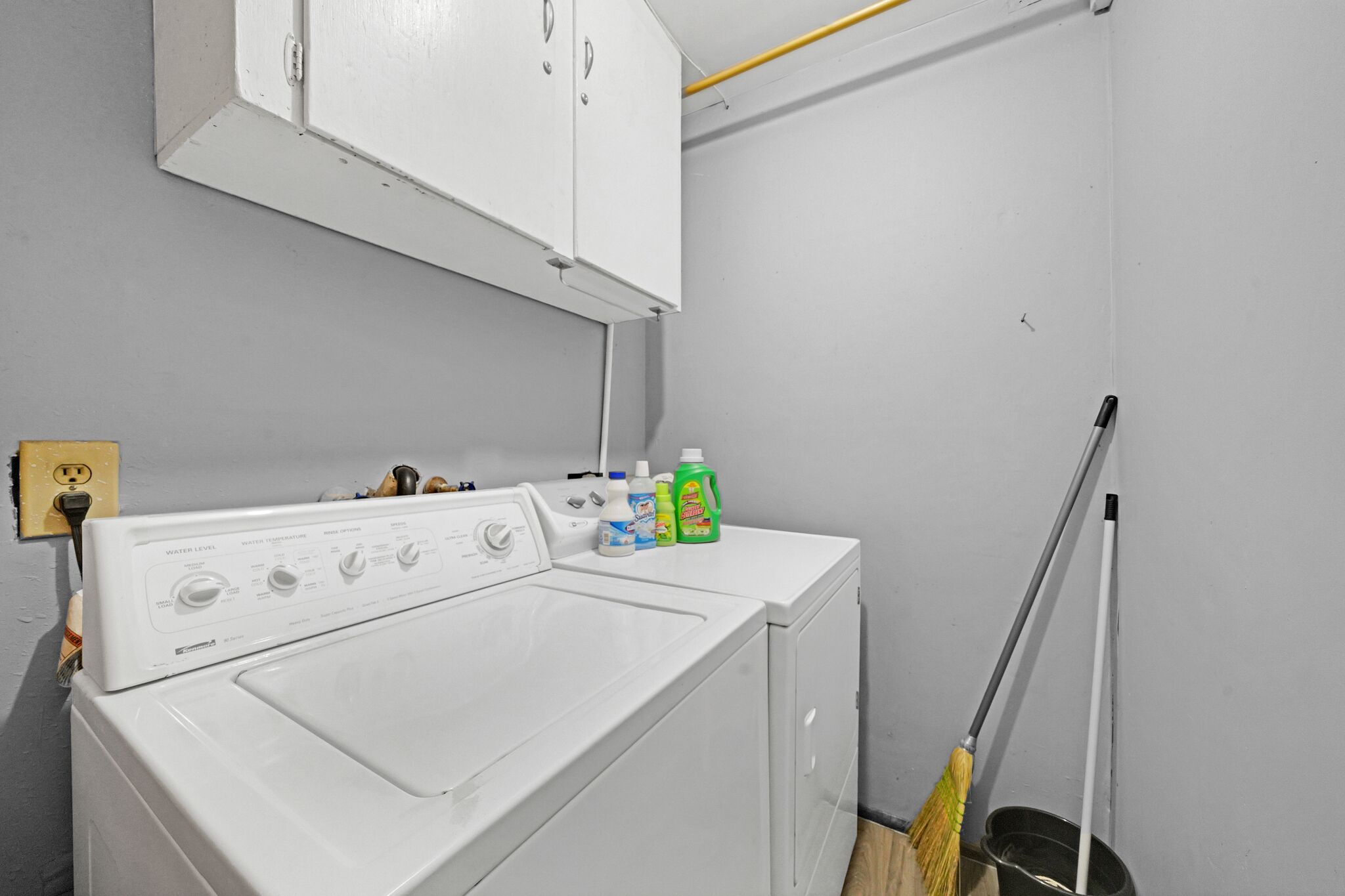 A laundry area with a front-loading washer and dryer, a mop, and cleaning supplies.