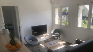 Una sala de estar moderna con un televisor de pantalla plana, dos sillones, un sofá, una mesa de centro y un comedor con un frutero.