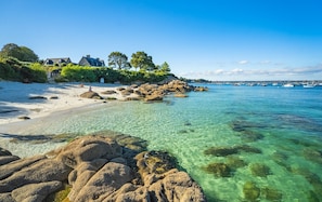 A coastal scene with clear waters, rocky shore, and a building with a garden.