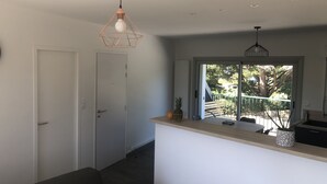 Una cocina moderna con una isla central, una puerta corrediza de vidrio a un balcón y una lámpara colgante de diseño geométrico.