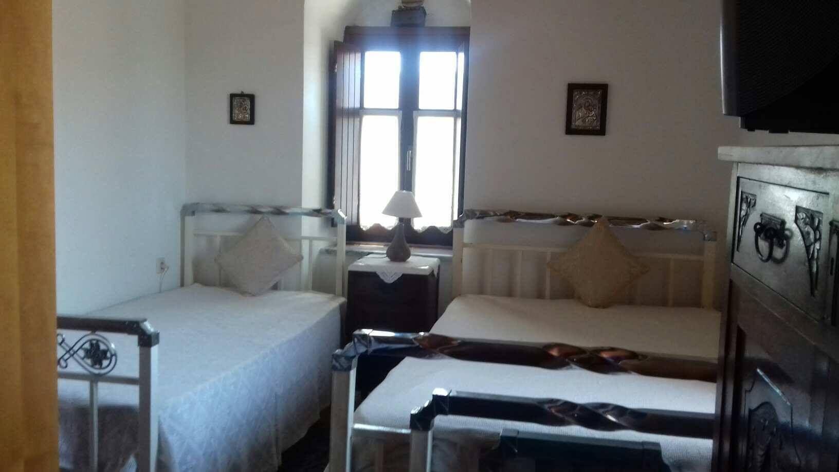 Een kamer met twee enkele bedden, een nachtkastje met een lamp, een radiator en een televisie.