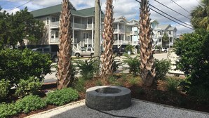 Una propiedad frente a la playa con edificios de varios pisos, un jardín ajardinado con palmeras y un pozo de fuego.