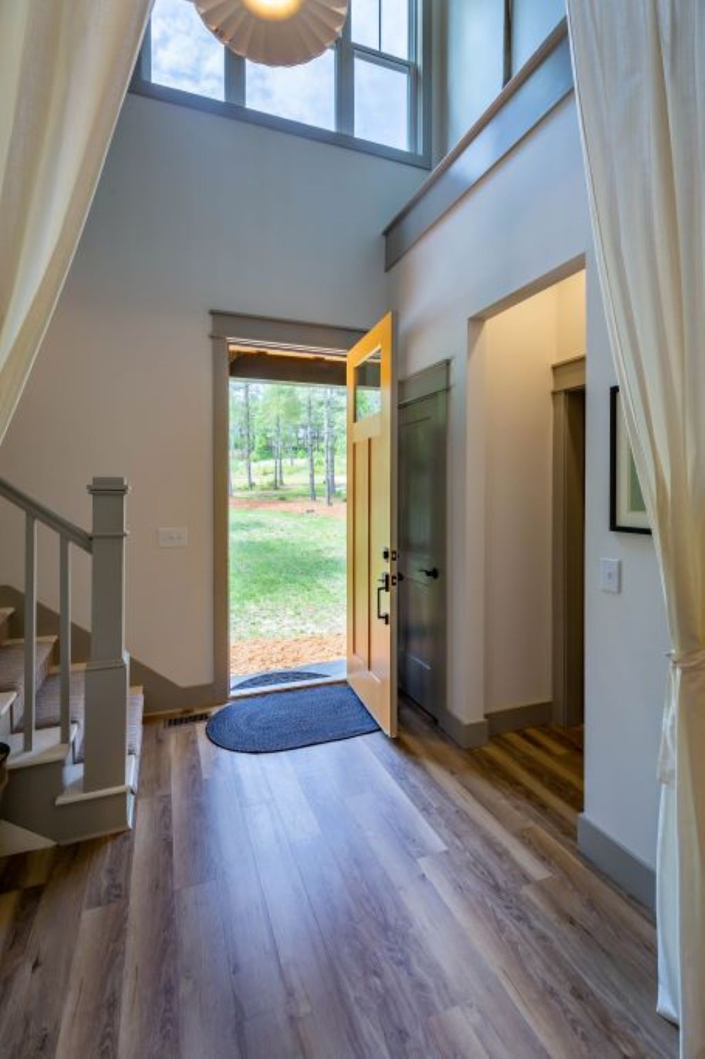 A spacious hallway with a wooden floor, a door leading outside, and a staircase on the left.