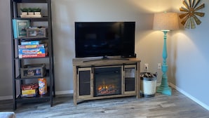 A living room with a TV on a wooden stand, a bookshelf with board games, a fireplace, and a teal lamp. - ••Newly remodeled and family friendly! AMAZING Strip views & close to it ALL!! (Branson)