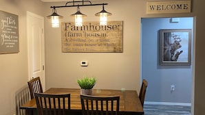 A dining area with a wooden table and chairs, a 'Welcome' sign, a 'Farmhouse' sign, and a framed painting of a cow. - ••Newly remodeled and family friendly! AMAZING Strip views & close to it ALL!! (Branson)