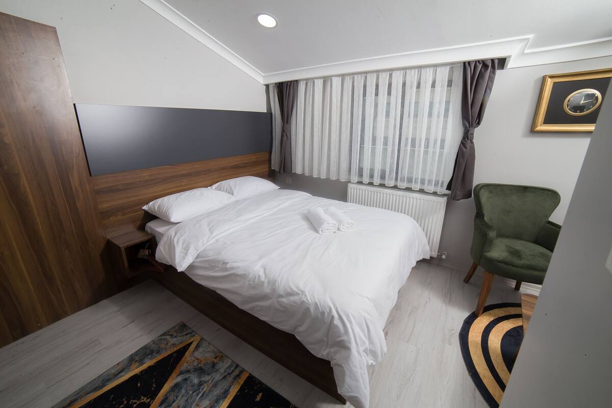 A modern hotel room with a large bed, a green armchair, and a window with sheer curtains.