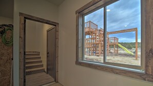 Una escalera lleva a una puerta de madera, un ventanal ofrece vista a un parque infantil y una pared con cableado eléctrico.
