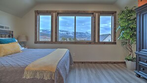 Un dormitorio con un ventanal grande, una cama con colcha acolchada, una lámpara de noche y una planta en maceta.