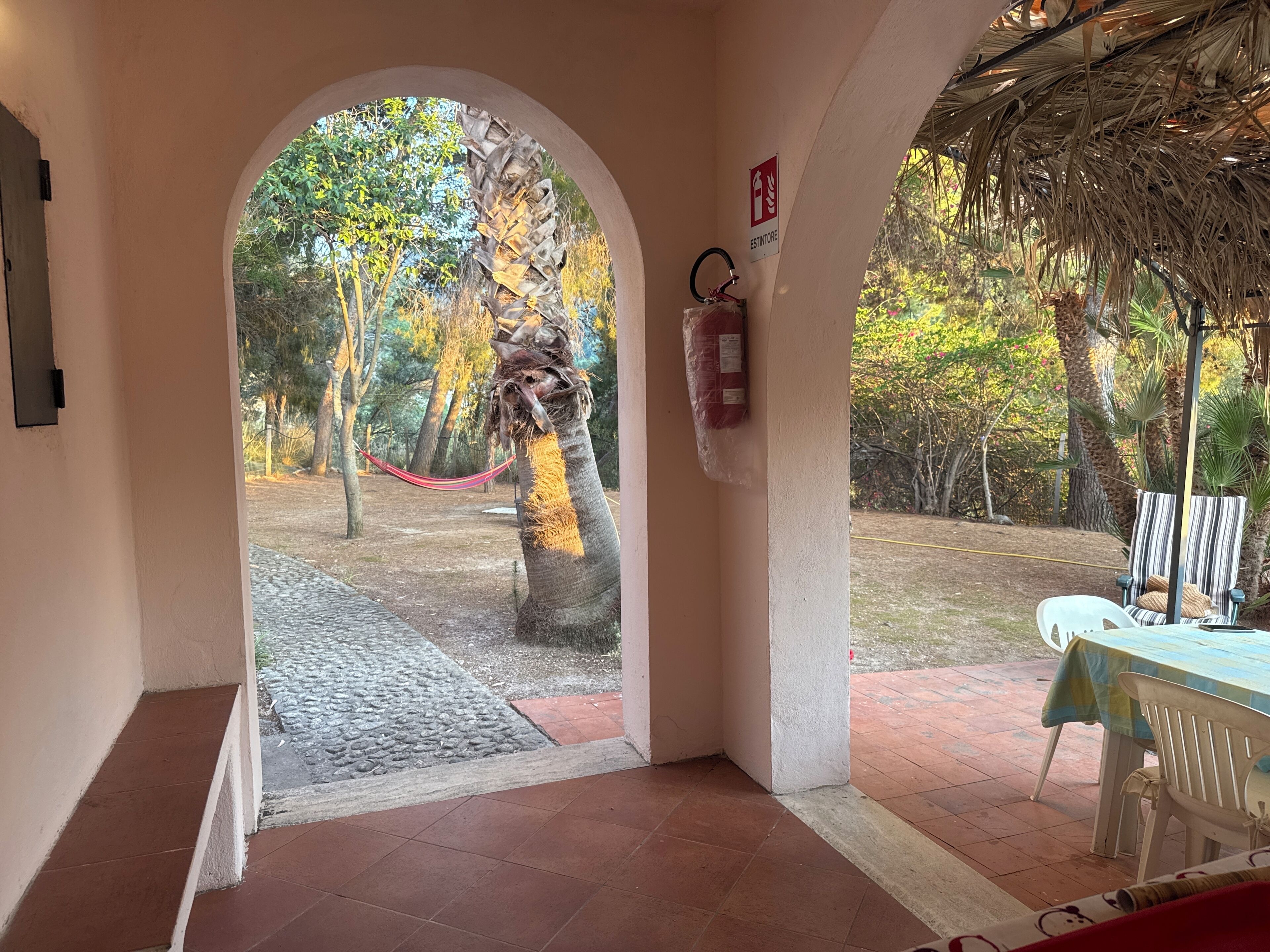 An arched doorway leading to an outdoor area with a hammock, a fire extinguisher, and a table with chairs.