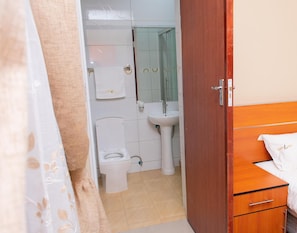 A bathroom with a toilet, sink, and wooden cabinet. - Travelodge Malawi (Blantyre)