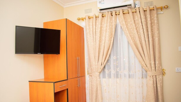 A bedroom with a bed, a wardrobe, a flat-screen TV, and a window with curtains.