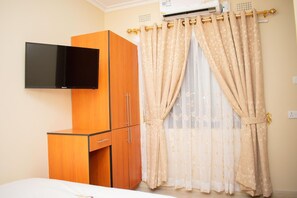 Un dormitorio con cama, armario, televisor de pantalla plana y ventana con cortinas.