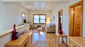 A spacious living area with a sofa, a coffee table, and a wooden bench. There is a window with blinds, a door, and a small table with a vase. -  Loft @ 420 on Chestnut (Mount Shasta)