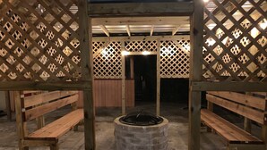 A covered outdoor seating area with wooden benches and a central fire pit.