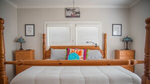 A bedroom with a wooden four-poster bed, white bedding, two nightstands with lamps, and a window with blinds.