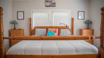 A bedroom with a wooden four-poster bed, white bedding, two nightstands with lamps, and a window with blinds.