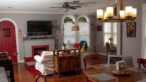 A dining area with a wooden table, chairs, and a bench. There is a fireplace with a red door, a television mounted above it, and a ceiling fan.