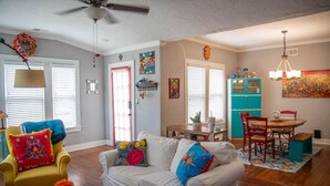 A living room with a white sofa, yellow armchair, and a dining area with a turquoise cabinet and red chairs.