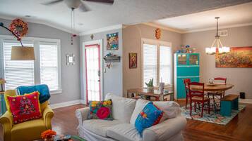 A living room with a white sofa, yellow armchair, and a dining area with a turquoise cabinet and red chairs.