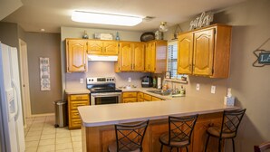 A kitchen with wooden cabinets, a central island with bar stools, a stainless steel sink, and a refrigerator. - Sunrise Shores - Waterfront Cottage sleeps 8.   (Chandler)