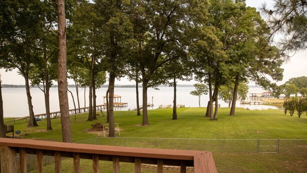 A grassy area with trees and a wooden deck overlooking a body of water. - Sunrise Shores - Waterfront Cottage sleeps 8.   (Chandler)