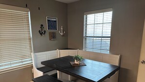A dining area with a dark wooden table and bench, white paneled walls, and a window with blinds. - Sunrise Shores - Waterfront Cottage sleeps 8.   (Chandler)