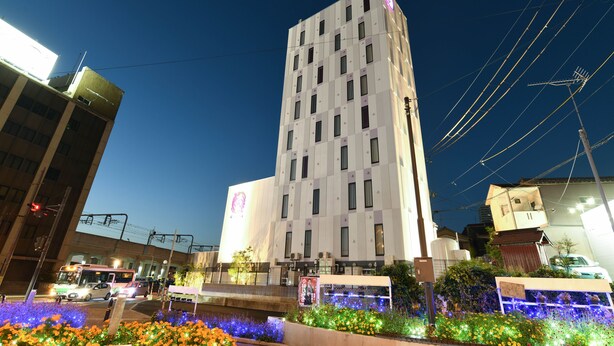 A modern building with a prominent logo, surrounded by a flower bed with colorful lights. - Hotel Wisteria Nara (Nara)
