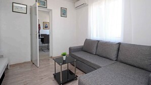 A modern living room with a grey sofa, a glass coffee table, and a small potted plant. There is a door leading to another room, and an air conditioning unit is mounted on the wall. - Holiday apartment with air conditioning near the beach (Baška)