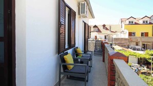 A balcony with two chairs and a table, overlooking a residential area with houses and a garden. - Holiday apartment with air conditioning near the beach (Baška)