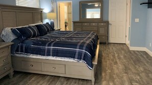 Een slaapkamer met een bed, een dressoir, een spiegel en een plafondventilator.