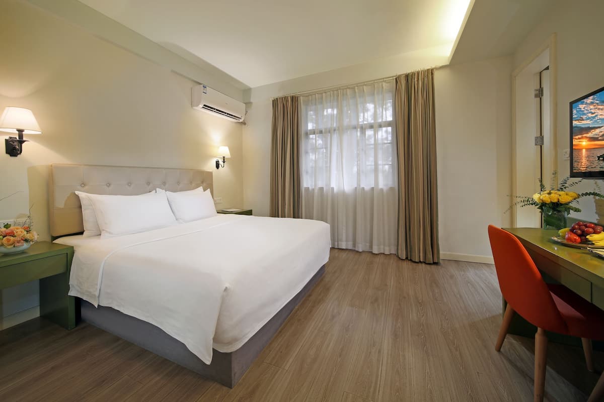 A hotel room with a large bed, a desk with a chair, a flat-screen TV, and a window with curtains.