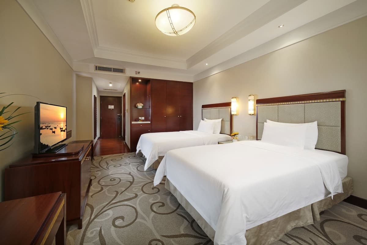 A hotel room with two beds, a television, a desk, and a decorative vase.