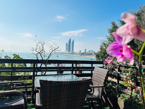 A balcony with wicker furniture overlooking a body of water and a cityscape.