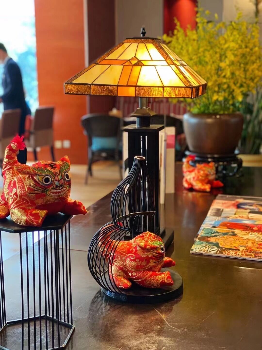 Una mesa con una lámpara decorativa, dos figuritas de rana y una revista.