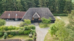 A large, thatched-roof building surrounded by lush greenery and a gravel driveway. - Great Higham Barn by Bloom Stays -  sleeps 26 guests  in 7 bedrooms (Sittingbourne)
