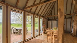 A spacious room with large windows, wooden beams, and a dining area with chairs and a table. - Great Higham Barn by Bloom Stays -  sleeps 26 guests  in 7 bedrooms (Sittingbourne)