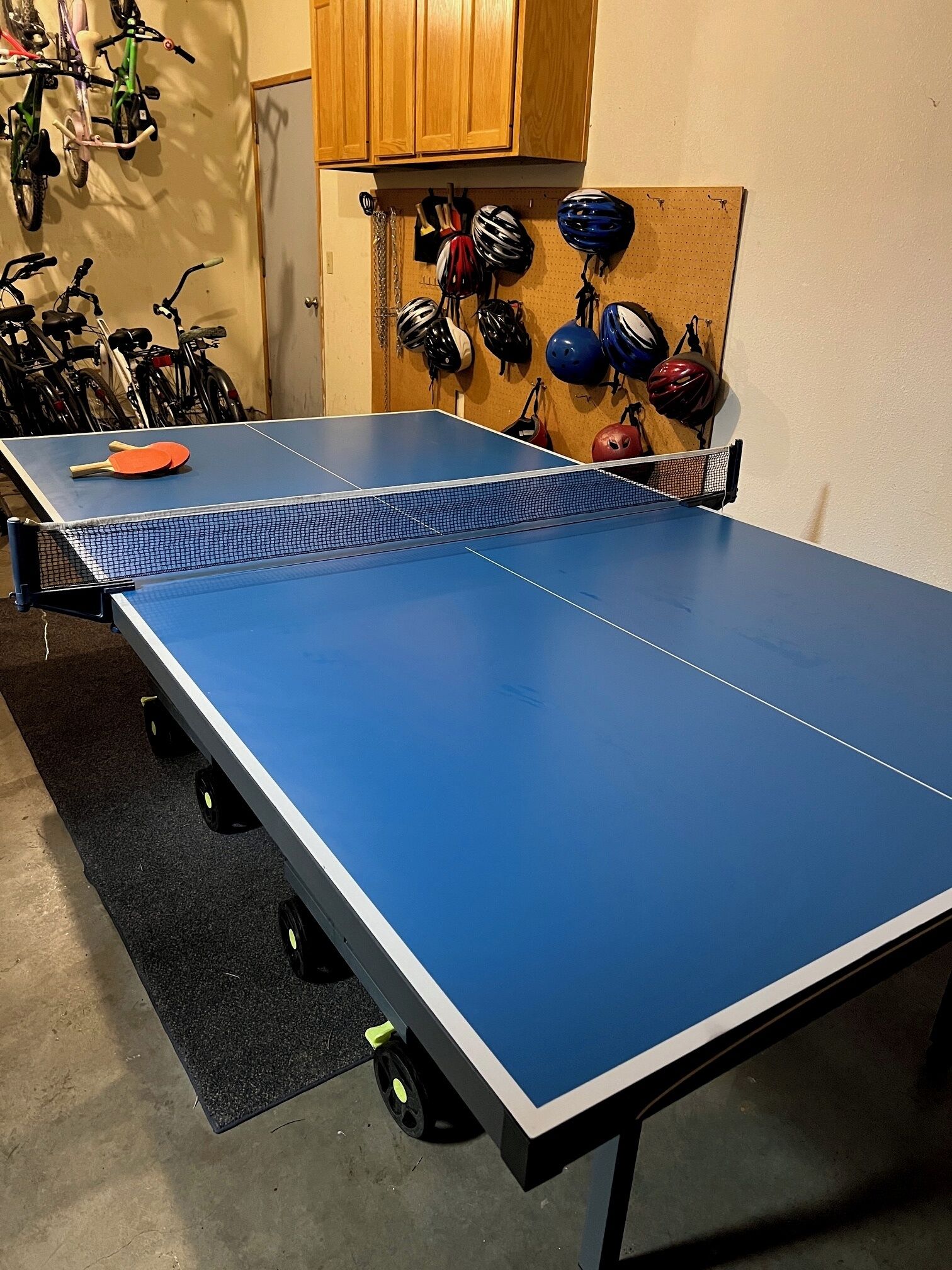Una mesa de ping pong en una habitación con bicicletas y cascos en la pared.