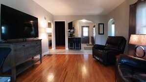 A spacious living room with a flat-screen TV, leather sofa, and a dining area in the background. - Single Level Living with Comfortable Recliners (Rochester)