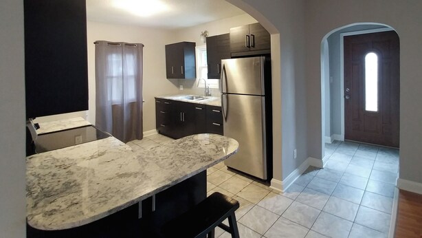 A kitchen with a marble countertop, stainless steel appliances, dark cabinets, and a tiled floor. - Single Level Living with Comfortable Recliners (Rochester)
