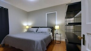 A bedroom with a bed, bedside lamps, a window with blinds, a black wardrobe, and a door with a brass handle. - Single Level Living with Comfortable Recliners (Rochester)
