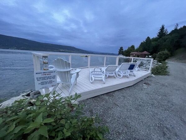 A deck with white lounge chairs and a sign indicating beach area closure at 11 PM daily. - "Together On The Lake" at La Casa Resort (Kelowna)