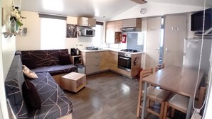 Cocina compacta para vehículos recreativos, con comedor, pequeña cocina y sala de estar con sofá y mesa de centro.
